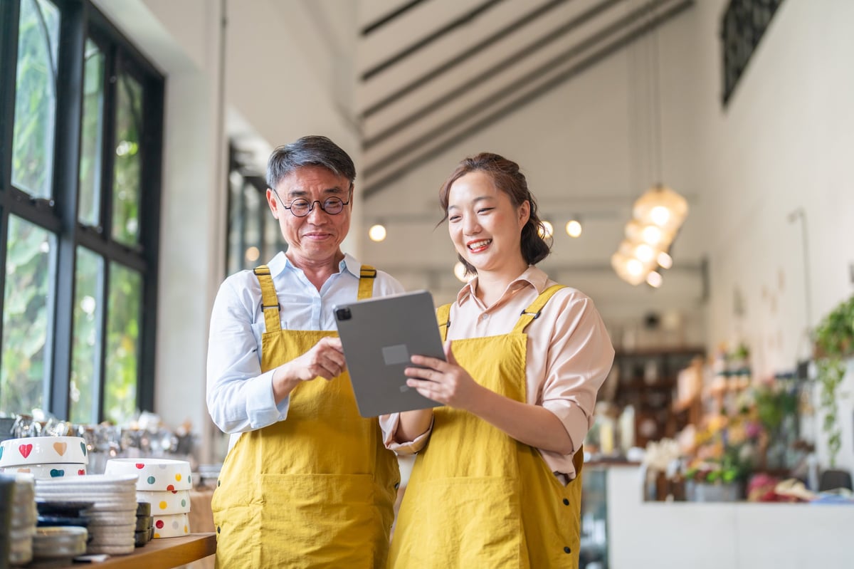Senior happy asian man and young woman in aprons running family small business checking ceramic stock, authentic local shop