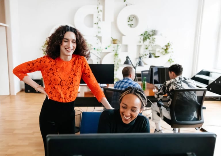Woman in orange lace top smiling at desk with child in modern office environment with colleagues working in background