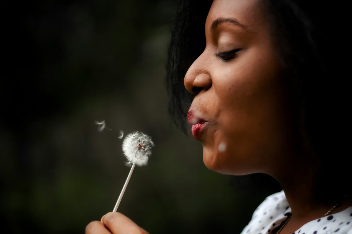 Woman blowing dandelion seeds into the air outdoors in profile view
