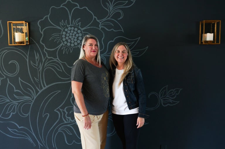 Man and woman standing together in front of a dark wall with ornate floral chalk drawings and small lit wall sconces